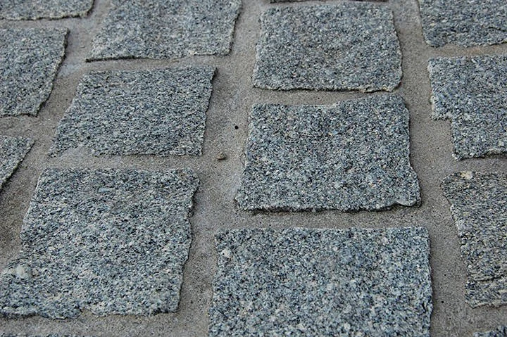 Peças pequenas de pedra cinza, com textura pontilhada, assentadas com juntas visíveis.