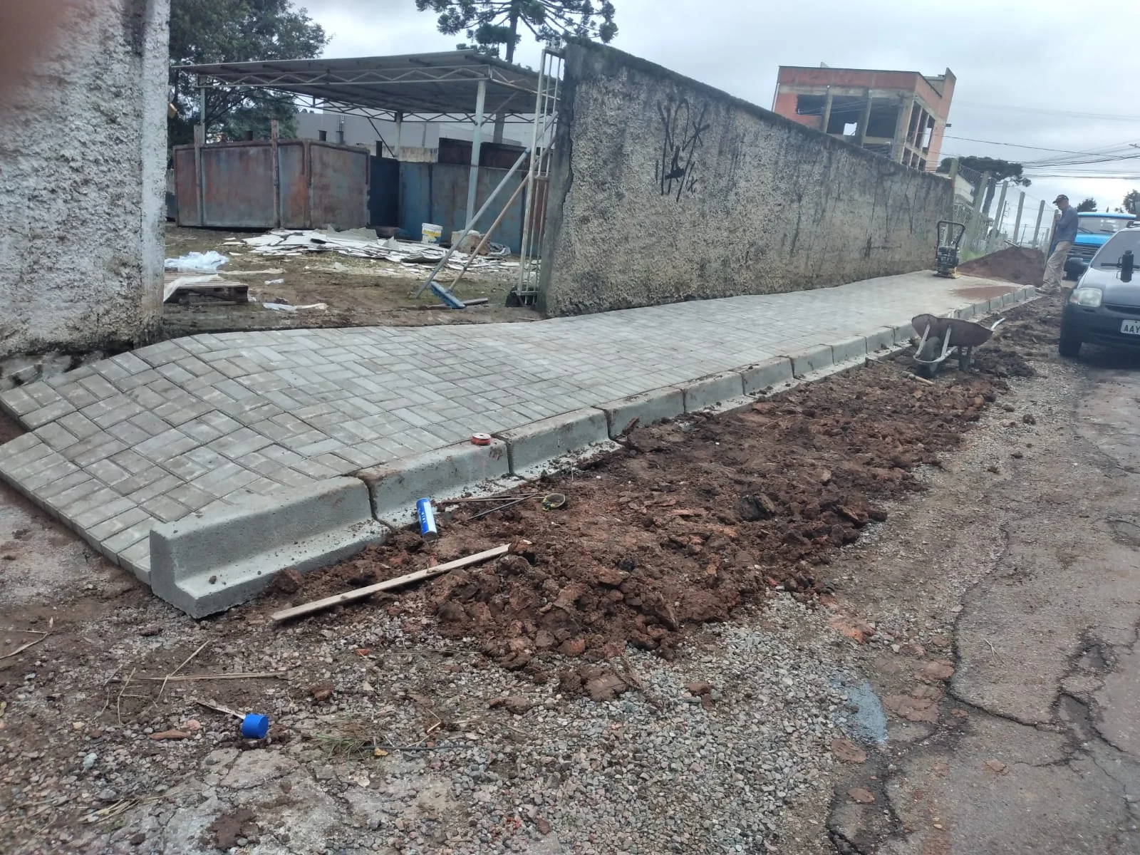 Passeio de peças retangulares junto a meio-fio e terreno em intervenção.