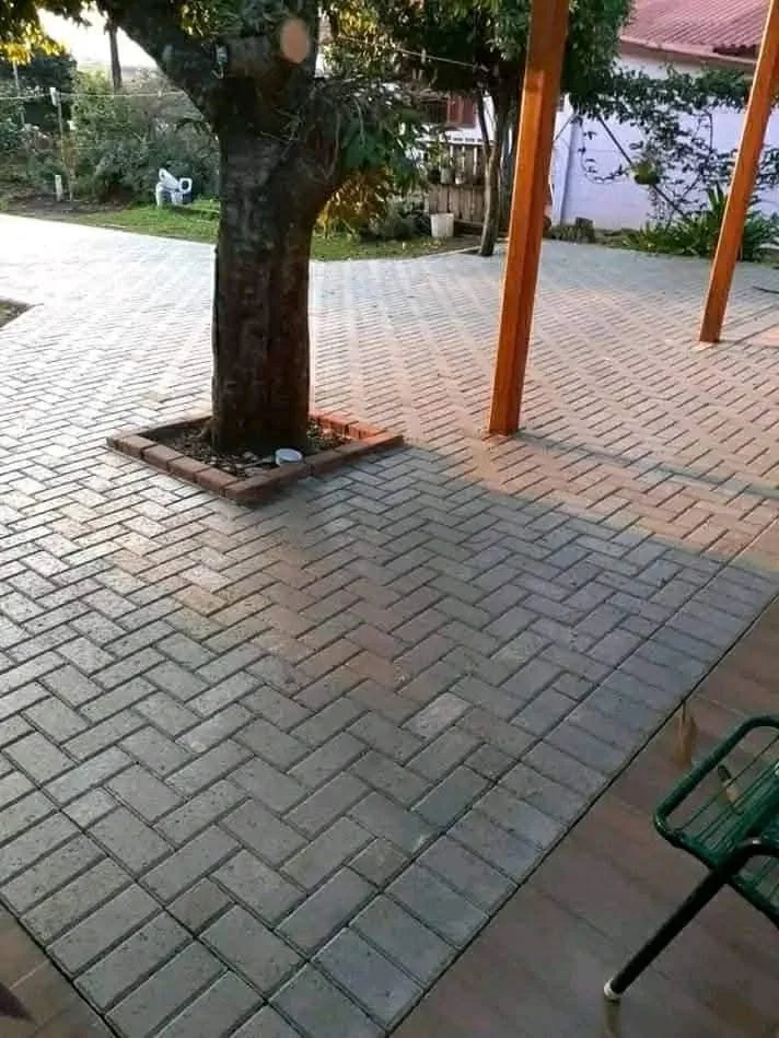Piso intertravado com juntas visíveis ao redor de árvore e pilares em área externa.