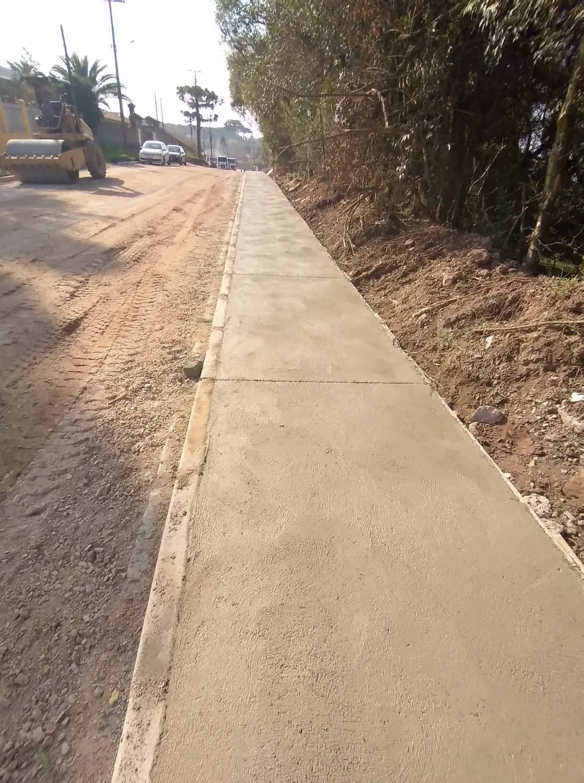 Passeio contínuo de concreto junto a via em preparação e equipamento de obra.