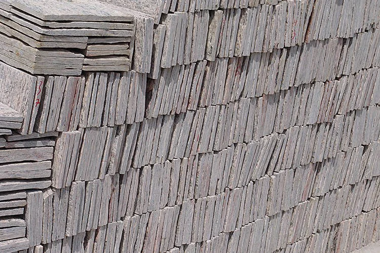Placas finas de pedra empilhadas verticalmente, em tons mesclados de cinza e rosa.
