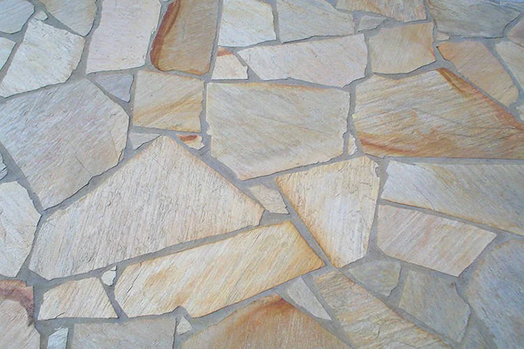Peças irregulares claras e amareladas formando um mosaico com juntas cinzas.